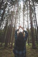 Happy woman in a plaid shirt enjoying the serenity of a dense forest, surrounded by tall trees, feeling freedom and connection with nature photo