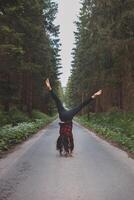 Acrobatic woman in black leggings and plaid shirt performs a cartwheel on a forest path in the middle of a deep forest. Coordination and agility training photo