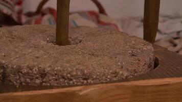 The ancient Quern stone hand mill with grain. The man grinds the grain into flour with the help of a millstone. Men hands on a millstone. Old grinding stones turned by hands video