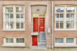A red door is open in front of a brick building photo