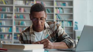 African American man working studying laptop desktop computer e-learning education male student copying writing notebook looking monitor preparing exam guy library technology knowledge college diploma video