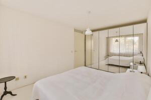 A white bedroom with a bed and a mirror photo