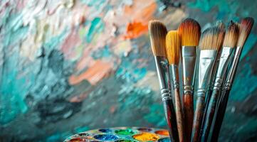 A collection of paintbrushes resting on a palette in front of a colorful abstract canvas photo