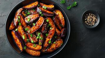Delicious roasted eggplant wedges garnished with green onions served in a black bowl photo