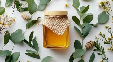 Fresh honey surrounded by green eucalyptus leaves and white flowers on a light surface photo