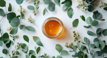 Fresh honey surrounded by green eucalyptus leaves and white flowers on a light surface photo