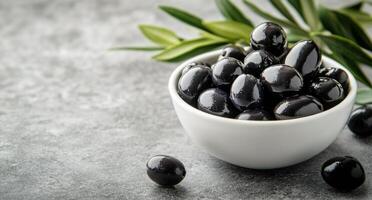 Fresh black olives served in a white bowl with olive leaves on a textured gray surface photo