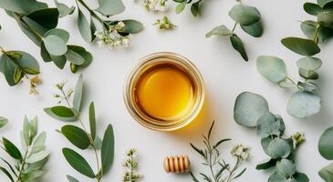 Fresh honey surrounded by green eucalyptus leaves and white flowers on a light surface photo