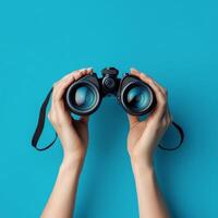 Hands holding binoculars against a vibrant blue background showcasing a sense of exploration photo