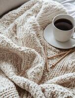 Cozy cup of coffee on knitted blanket with wooden knitting needles resting nearby photo