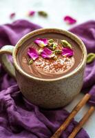 Warm spiced cocoa topped with rose petals and nuts resting on a purple cloth photo