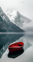 un solitario rojo barco anclado en calma aguas rodeado por brumoso cubierto de nieve montañas foto