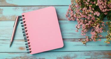 A pink notebook and pen with flowers on a blue wooden table in a cozy setting photo