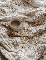 Cozy cup of coffee on knitted blanket with wooden knitting needles resting nearby photo