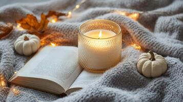 Cozy autumn evening with a lit candle, small pumpkins, and a book on a warm knitted blanket photo