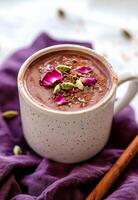 Warm spiced cocoa topped with rose petals and nuts resting on a purple cloth photo