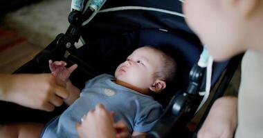 Handheld selective focus shot, Two happy women playing with a little boy lying in a baby stroller. Family enjoying happy time together. Happy lifestyle. video