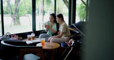 Handheld wide view shot, Two happy siblings sit at a table playing social media together on smartphone while waiting for little boy to wake up. Family enjoying happy time together. video