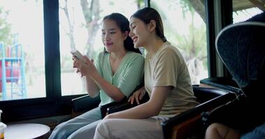 Handheld selective focus shot, Two happy siblings sit at a table playing social media together on smartphone while waiting for little boy to wake up. Family enjoying happy time together. video