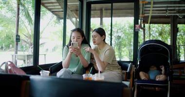 Handheld wide view shot, Two happy siblings sit at a table playing social media together on smartphone while waiting for little boy to wake up. Family enjoying happy time together. video