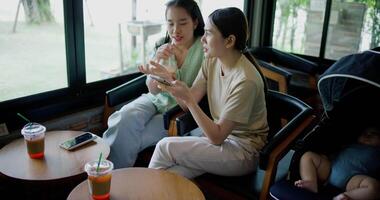 Handheld high angle view shot, Two siblings happily sit at a table, drinking cold drinks while playing social media together on smartphone at a coffee shop. Family enjoying happy time together. video