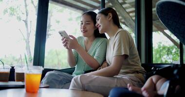 Handheld selective focus shot, Two siblings are playing social media together on smartphone while sitting at a table in a cafe. Family enjoying happy time together. video