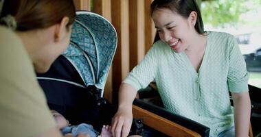 Handheld selective focus shot, Two happy women playing with a little boy lying in a baby stroller. Family enjoying happy time together. Happy lifestyle. video
