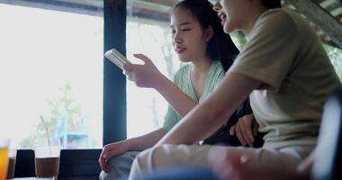 Handheld low angle view shot, Two siblings are playing social media together on smartphone while sitting at a table in a cafe. Family enjoying happy time together. video