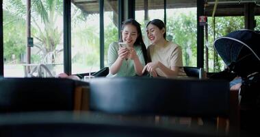 Handheld wide view shot, Two happy siblings sit at a table playing social media together on smartphone while waiting for little boy to wake up. Family enjoying happy time together. video