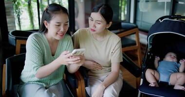 Handheld selective focus shot, Two happy siblings sit at a table playing social media together on smartphone while waiting for little boy to wake up. Family enjoying happy time together. video
