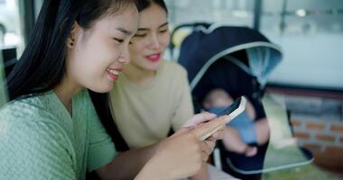 Handheld selective focus shot, Two happy siblings sit at a table playing social media together on smartphone while waiting for little boy to wake up. Family enjoying happy time together. video
