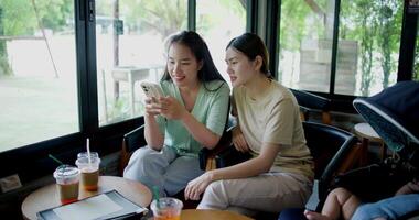 Handheld wide view shot, Two happy siblings sit at a table playing social media together on smartphone while waiting for little boy to wake up. Family enjoying happy time together. video