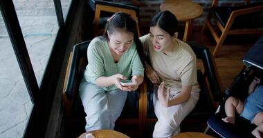Handheld high angle view shot, Two happy siblings sit at a table playing social media together on smartphone while waiting for little boy to wake up. Family enjoying happy time together. video