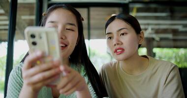 Handheld selective focus shot, Two siblings are playing social media together on smartphone while sitting at a table in a cafe. Family enjoying happy time together. video