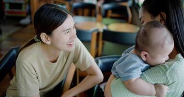 Handheld high angle view shot, Two happy women having fun playing with a little boy in a coffee shop. Family enjoying time together. Happy lifestyle. video