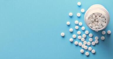 White pills spilled from an overturned bottle on a light blue background photo