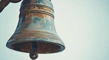 Rustic bronze bell hanging from a branch with blurred background of autumn leaves during daylight photo