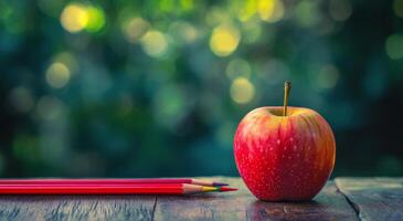 Bright red apple next to colorful pencils on a wooden table in a garden setting photo