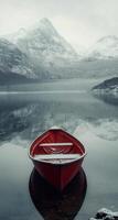A solitary red boat anchored in calm waters surrounded by misty snow-covered mountains photo