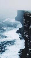 Rugged cliffs meet turbulent waves on a misty day at the shoreline photo