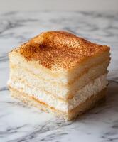 Delicious layer of whipped cream and cake dusted with cocoa served on a marble countertop photo