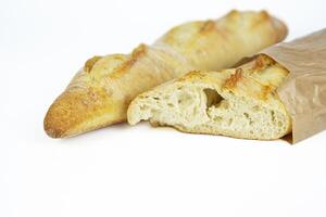 Two freshly baked baguettes, one wrapped in brown paper bag, Artisan French baguettes with crispy crusts in paper packaging. Isolated on a white background. Closeup. With clipping path. Copy space photo