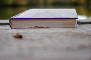 Closed book on the lake wooden dock on autumn day. Reading and learning enjoying tranquility of nature. Peaceful outdoor environment. Selective focus. Blurred background. photo