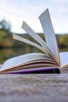 Open book with pages flipping in the wind. Reading on the lake wooden dock on autumn day. Learning enjoying tranquility of nature. Peaceful outdoor environment. Selective focus. Blurred background. photo
