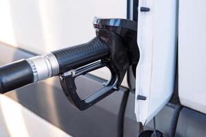 Closeup of a fuel nozzle in the car tank. Process of refilling a white transporter bus at a gas station. Refueling pistol inserted into a vehicle at a gas station. Copy space photo
