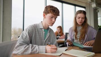 University students sitting together at table with books and laptop video