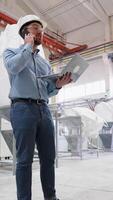Chief engineer of pvc windows factory speaks on phone and using a laptop on production line. Vertical video
