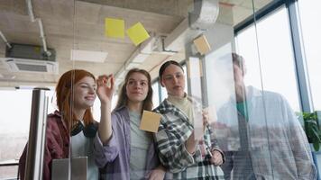 Group of students while working together during brainstorming and standing behind glass wall with sticky colorful papers video