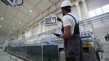 Factory worker in a hard hat and uniform is using a tablet with an engineering software video