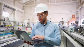 Factory chief engineer in a hard hat is using a laptop with an engineering software video